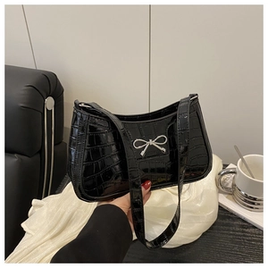 Close-up of black crocodile embossed patent leather bag with silver metal bow detail