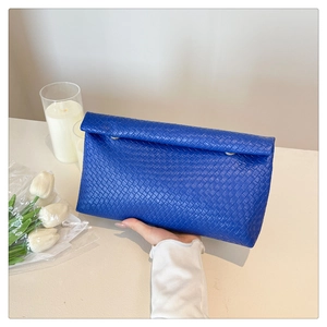 Close-up of a blue woven leather envelope clutch held in a clean, elegant setting