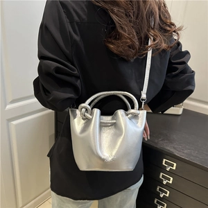 Silver pleated bucket bag with knot handle and shoulder strap shown in a lifestyle view