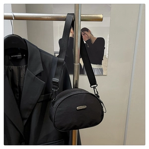Close-up of black nylon crescent crossbody bag with adjustable strap on suit jacket