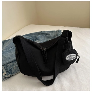 Detail of black nylon crescent bag with wide strap and round coin purse on white bedding