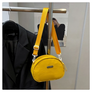 Detail of a bright yellow nylon crossbody bag featuring a metal logo plate and wide strap