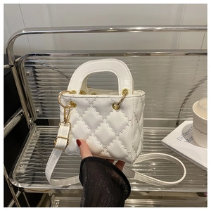 Detail of white quilted crossbody bag with top handle and metal hardware on a display stand