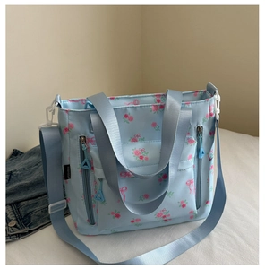 Detail of light blue floral tote bag with pink rose patterns and functional front pockets