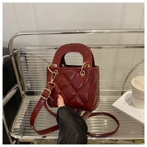 Detail of burgundy mini handbag with quilted pattern and gold metal hardware