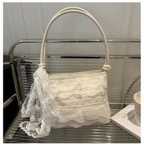 Close-up of cream lace shoulder bag with textured ruffles and decorative lace scarf