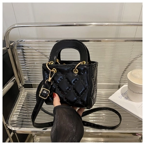 Detail of a black quilted patent leather mini tote bag with gold metal hardware on display