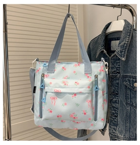 Detail of light blue floral tote bag with pink roses and bow prints featuring zip pockets