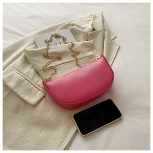 Pink lychee grain saddle bag with gold chain strap on beige blazer and book