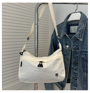 Detail of a creamy white nylon shoulder bag with a black triangular zipper puller and logo