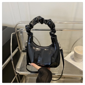 Detail of glossy black moon bag featuring pleated handle and fashion typography