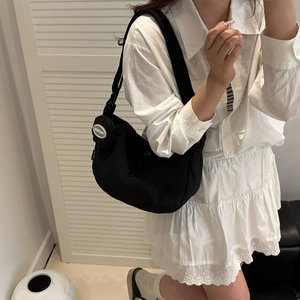 Minimalist black nylon crescent shoulder bag with small circular pendant on wide strap