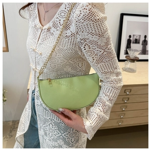 Close-up of light green lychee textured crescent bag with gold chain strap on model