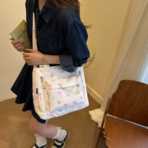 White canvas shoulder bag with pink floral and bow prints and multiple zipper pockets