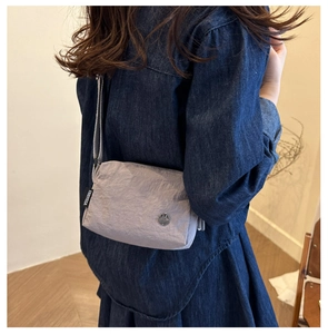 Detail of light grey pleated fabric bag with metal M logo and adjustable shoulder strap