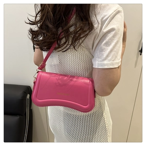 Close-up of bright magenta baguette bag featuring a unique wavy base and gold logo detail