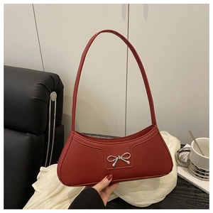 Detail of red leather baguette bag featuring a silver bow buckle on white fabric