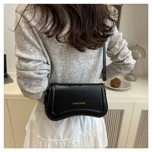 Detail of a black glossy leather crossbody bag showing retro minimalist design and strap