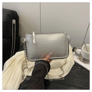 Détail d'un sac bandoulière argenté à motif crocodile avec chaîne et rivets ronds