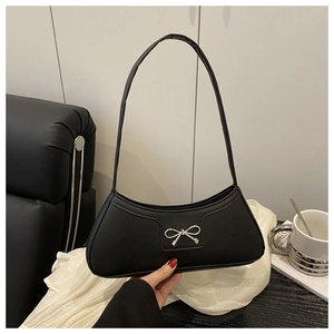 Detail of matte black baguette bag with silver metal bow on a leather sofa