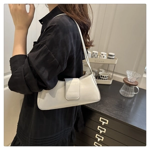 Side view of a creamy white leather baguette bag worn by a model in a modern home interior