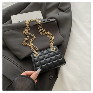 Detail of black quilted shoulder bag with chunky gold chain strap on grey blazer