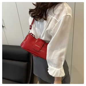 Close-up of the red patent leather shoulder bag with white branding and adjustable strap