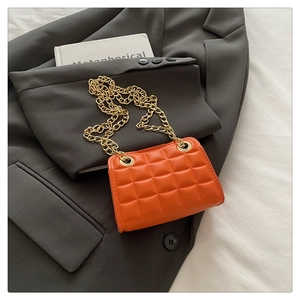 Detail of orange quilted crossbody bag with gold chain strap on a grey blazer