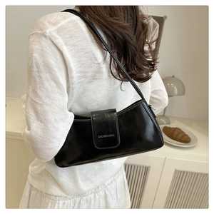 Close-up of shiny black patent leather baguette bag with flap and embossed logo