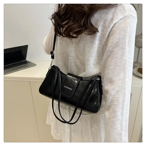 Side view of a black glossy underarm baguette bag with white lettering and silver buckle