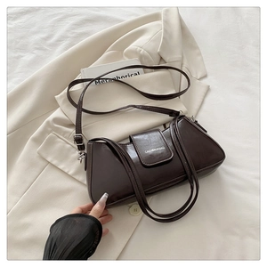 Detail of a deep coffee baguette bag with glossy patent leather finish on white fabric