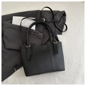 Detail of black pebbled leather bucket bag with light gold hardware and strap on a suit