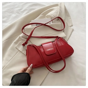 Detail of red synthetic leather handbag with embossed text on beige blazer background