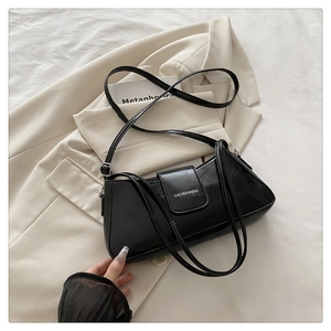 Detail of minimalist black baguette bag with adjustable straps on a beige blazer