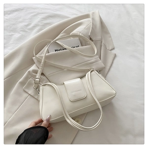 Detail shot of a creamy white leather underarm bag with a magnetic buckle and adjustable strap