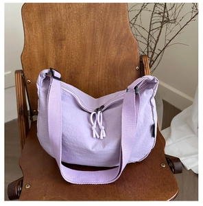 Detail of lavender crescent bag with woven zipper pulls on a rustic wood seat