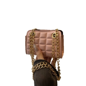 Pink quilted crossbody bag with gold chain strap held against white background