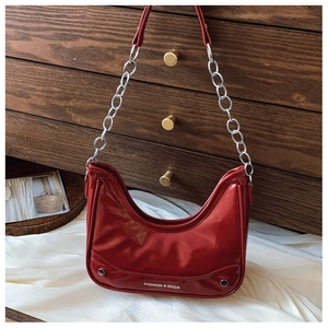 Close-up of red patent leather crescent bag with silver rivets and metal chain strap