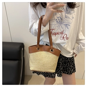 Detail of handwoven straw tote bag with brown leather handles and golden metal hardware