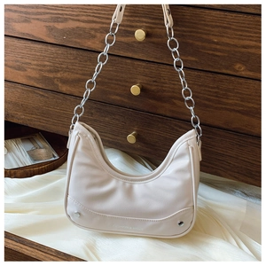 Close-up of cream crescent shoulder bag with silver chain on silk fabric
