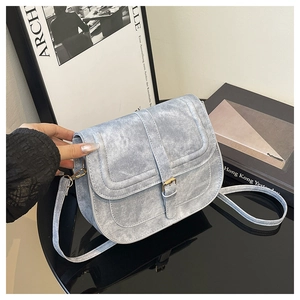 Detail of light blue corduroy saddle bag featuring gold buckle and textured fabric