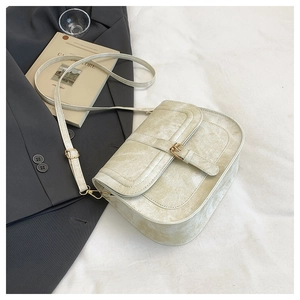 Detail of off-white crossbody saddle bag with marble texture and gold buckle hardware