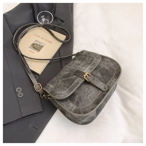 Close-up of grey vintage saddle bag with matte texture and gold buckle on a suit jacket