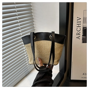 Detail of hand-held straw tote bag with black leather straps and contrasting trim