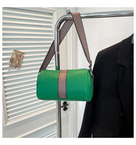 Detail einer grünen Zylindertasche aus genarbtem Leder mit gewebtem Schultergurt