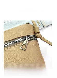 Close-up of smooth metal zipper and lychee grain leather on a brown crossbody bag