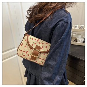 Detail of cherry print canvas bag with brown leather strap worn by a model