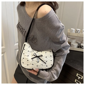 Détail du sac plissé blanc avec broderie nœud noir et pendentif cœur argent