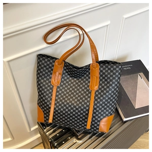 Détail d'un sac cabas à motifs géométriques avec poignées en cuir sur une valise