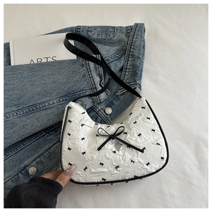 Détails du sac croissant blanc avec texture plissée, motifs nœuds et breloque cœur